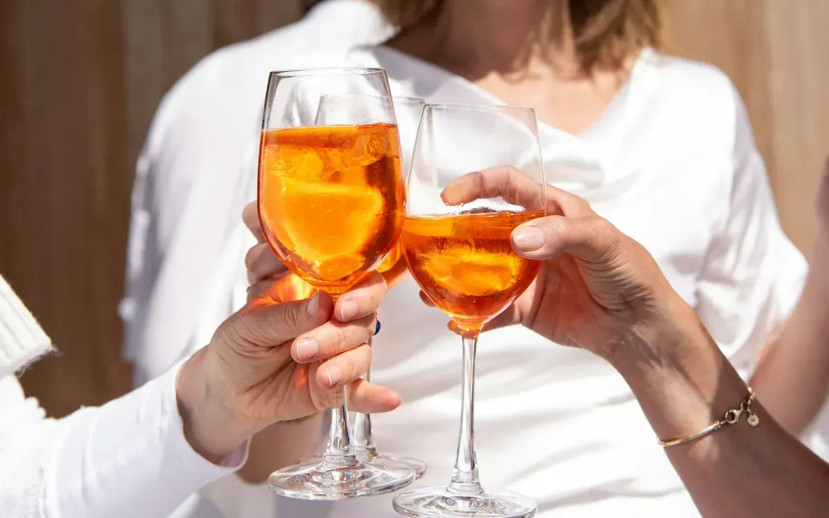 Zwei Gläser Aperitif in den Händen zweier Personen