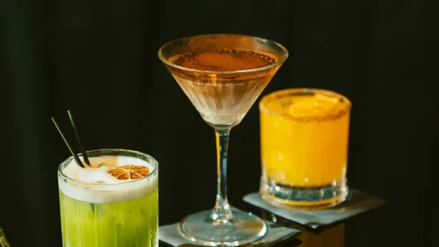 Drei bunte Cocktails auf einer dunklen, spiegelnden Bar – Swingerclub Preise und was im Eintritt steckt
