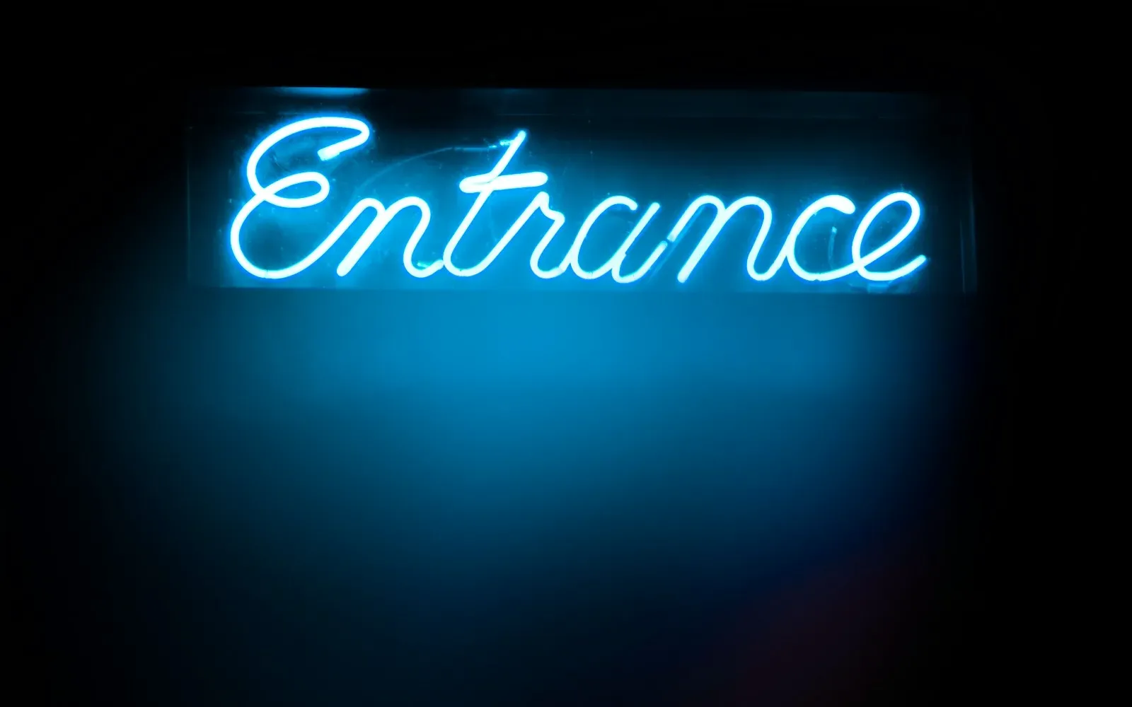 Leuchtende Neon-Schrift „Entrance“ an einer dunklen Wand